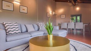 A modern living room with a grey sofa, a round gold coffee table, and a dining area with white chairs. - Villa Diana - Private Villa with pool (Provincia di Brescia)