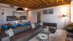 Ein modernes Wohnzimmer mit einem grauen Sofa, einem Essbereich mit blauen Stühlen und einer Küche im Hintergrund.