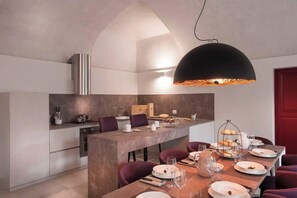 Una cocina moderna con una isla central, una zona de comedor con mesa de madera y una lámpara colgante negra.
