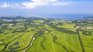 Luftaufnahme eines Golfplatzes mit mehreren Grüns, Wasserhindernissen und einem entfernten Gewässer.