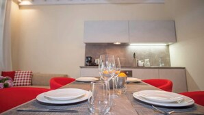 Uma área de refeições com uma mesa de madeira posta para quatro pessoas, incluindo pratos, copos e talheres.