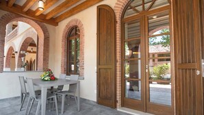 Um pátio externo com mesa e cadeiras, arcos de tijolo e portas de madeira.
