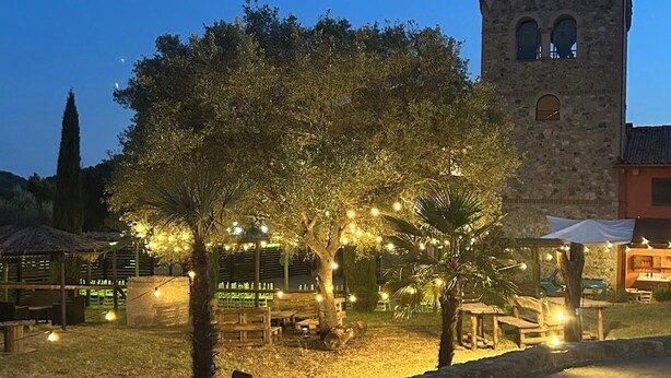 Une cour avec une tour en pierre, des arbres et des guirlandes lumineuses.