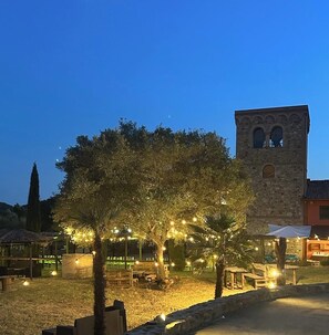 A courtyard with a stone tower, trees, and string lights. - Agriturismo La Fontanella & Glamping  (Suvereto)