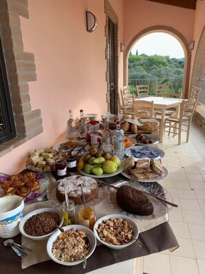 Una mesa dispuesta en un balcón con diversos alimentos, como pasteles, frutas y salsas.