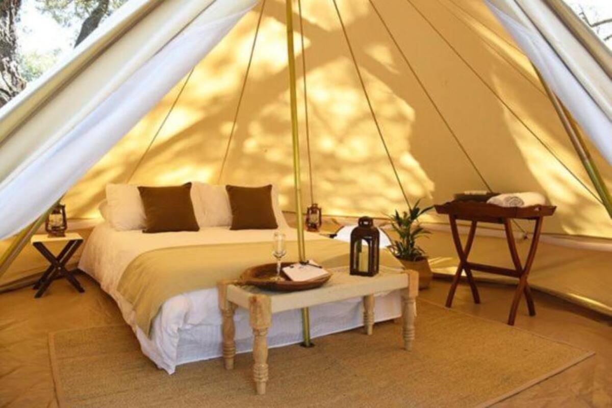 Una tienda de campaña con una cama, una mesita de noche y una pequeña mesa con un farol.
