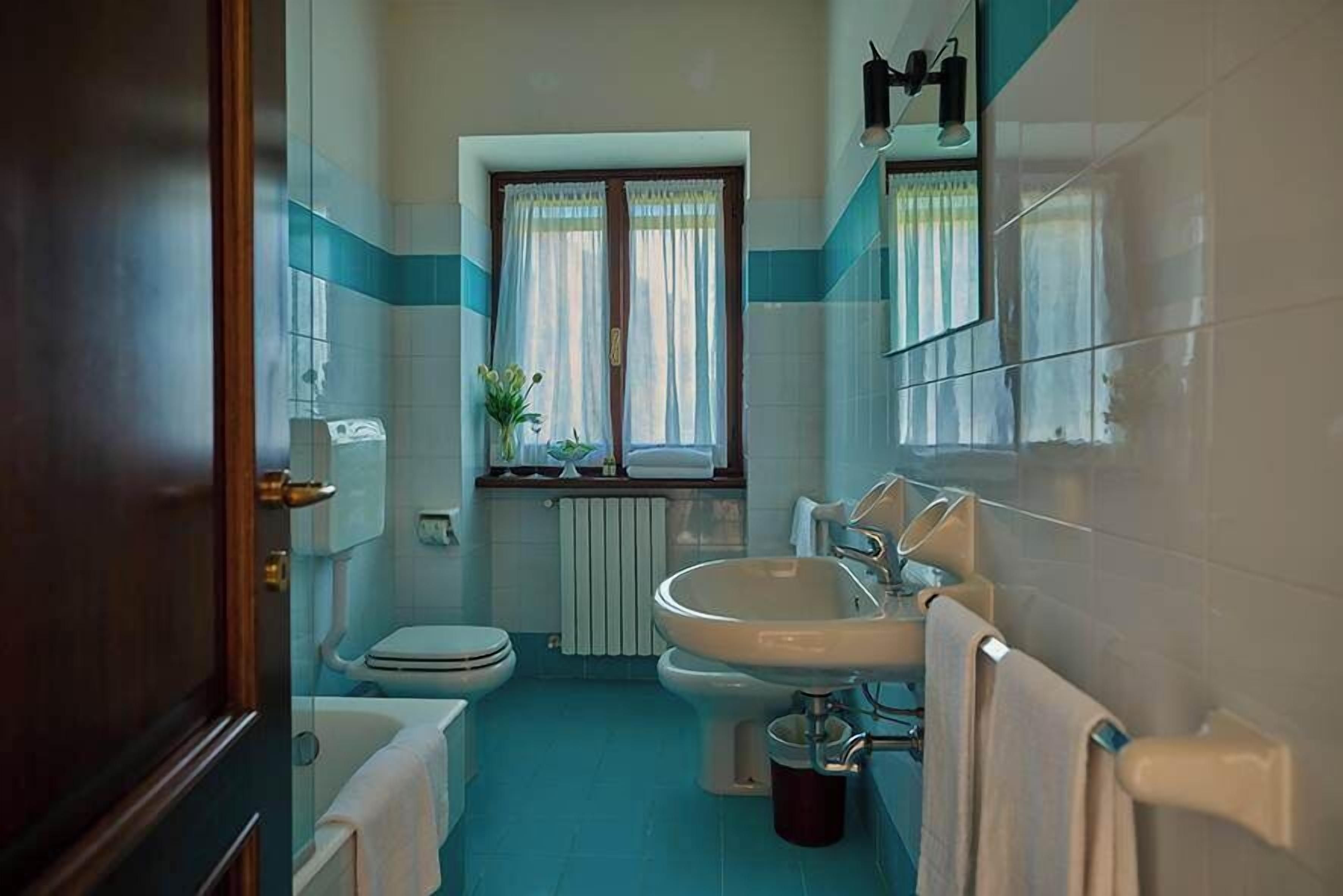 Un baño compacto con ba ñera, dos inodoros, un lavabo y una ventana con cortinas.