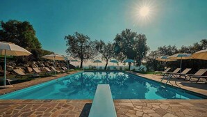 Ein Schwimmbecken mit Liegestühlen und Sonnenschirmen, umgeben von Steinplatten und Bäumen.