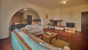 A living room with a sofa, coffee table, TV, fireplace, and an archway leading to a kitchen. - Villa Montecroce Apartment n.2 (Padenghe sul Garda)