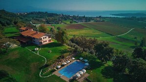 An aerial view of a large estate with a swimming pool, a tennis court, and a large house surrounded by fields and a body of water. - Villa Montecroce Apartment n.2 (Padenghe sul Garda)