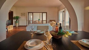 A dining area with a table set for four, a sofa in the background, and a view of a living room through an arched doorway. - Villa Montecroce Apartment n.2 (Padenghe sul Garda)