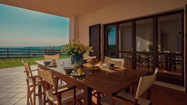 A dining area with a wooden table and chairs, a vase of flowers, and a view of the sea. - Villa Montecroce Apartment n.2 (Padenghe sul Garda)