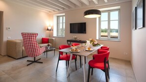 A modern living room with a sofa, a red and white patterned chair, a dining table with red chairs, a flat-screen TV, and a large window with a view. - Borgo di Drugolo Apartment n.9 (Drugolo)