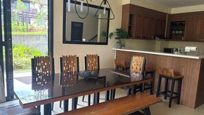 A modern kitchen with wooden cabinets, a central island, and a dining area with a glass table and wooden chairs.