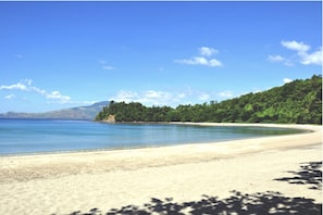 A beach with clear blue water, sandy shore, and green hills in the background.