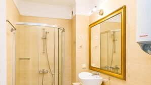 Un baño con ducha de vidrio, lavamanos blanco y un espejo grande.