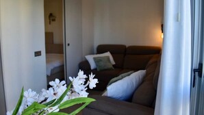 A modern hotel room with a sliding door leading to a bathroom, a dark brown sofa with cushions, and a small table with a vase of white flowers. - Luxury Apartment with Sea View, Perfect for Couples and Mature Guests (Dehesa de Campoamor)