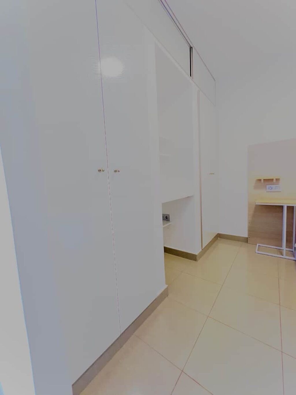 A room with white walls, a tiled floor, and a wooden desk with a chair.