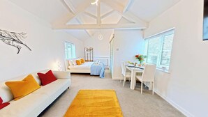 A modern, well-lit room with a white sofa, a dining table, and a yellow rug. - The Saddlery  -  a cottage that sleeps 2 guests  in 1 bedroom (Bridlington)