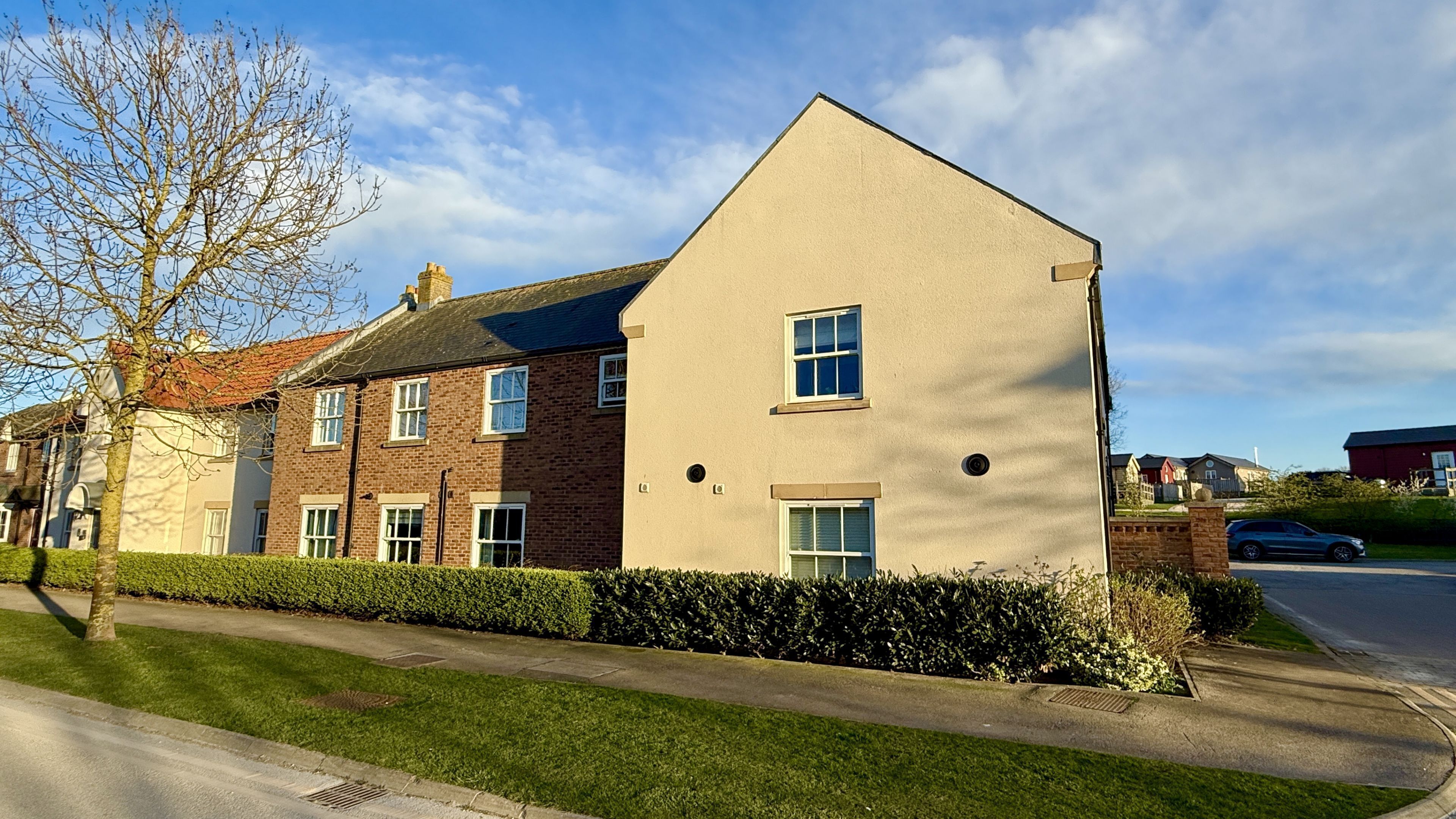 A residential building with a brick facade, multiple windows, and a well-maintained lawn.