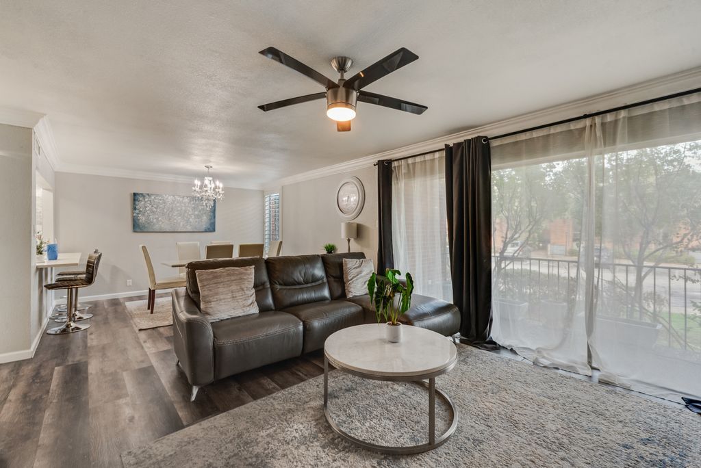 A living room with a dark leather sofa, a round coffee table, a ceiling fan, and a large window with curtains.