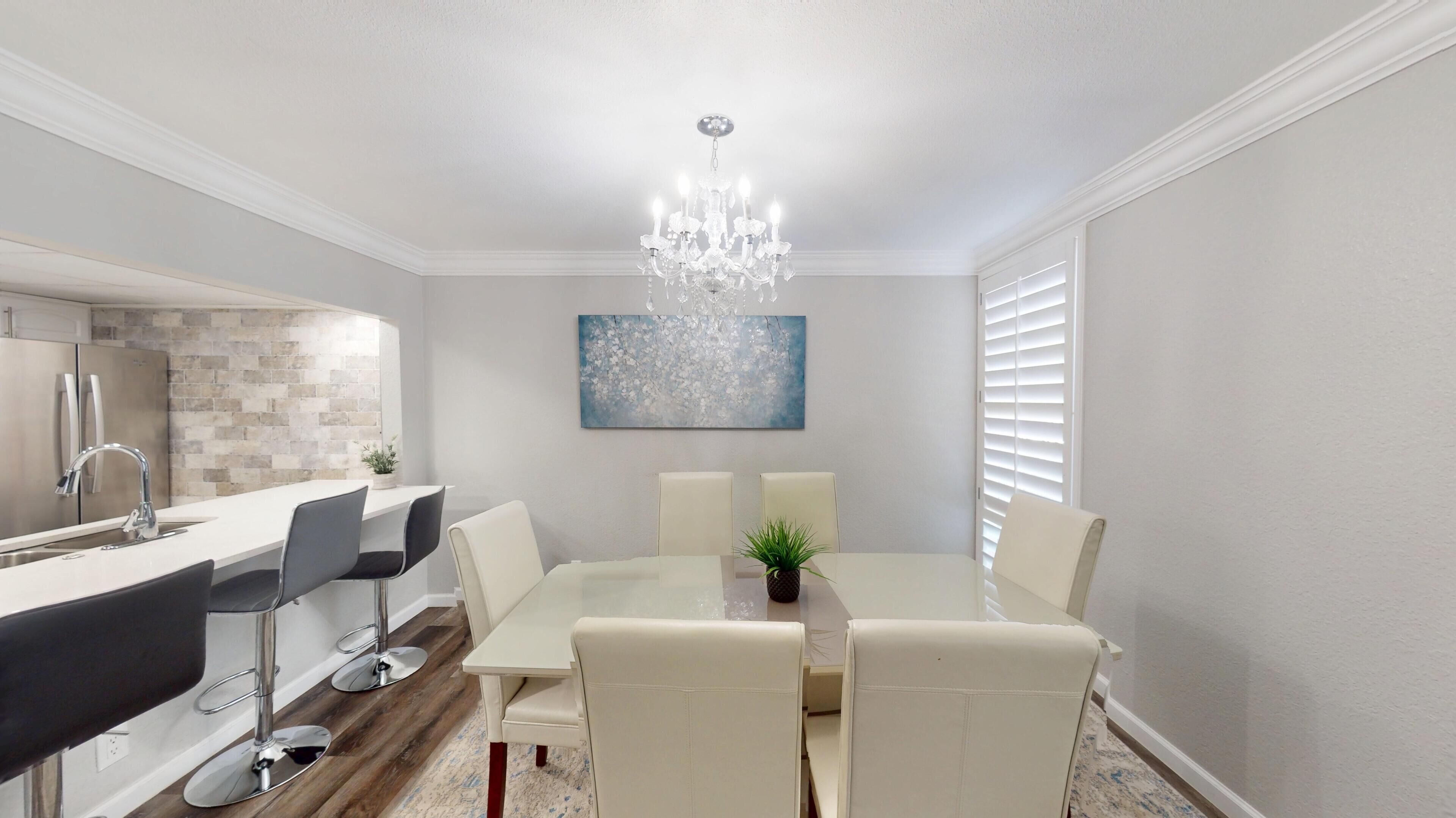 A modern dining area with a white table, six chairs, and a chandelier.