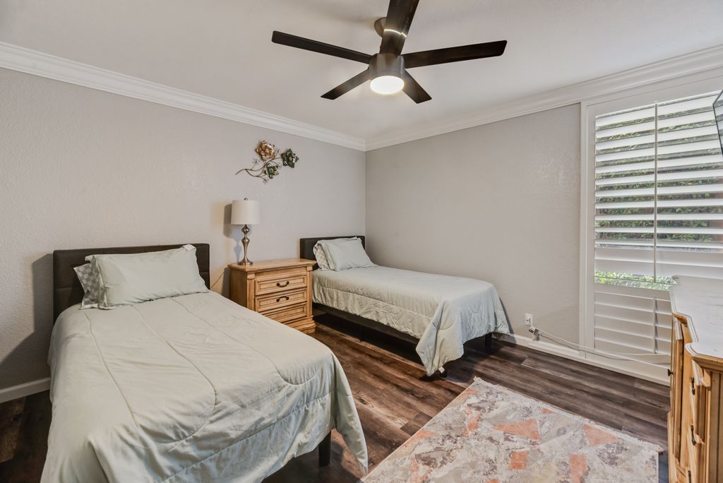 A bedroom with two beds, a ceiling fan, a nightstand, and a window with blinds.