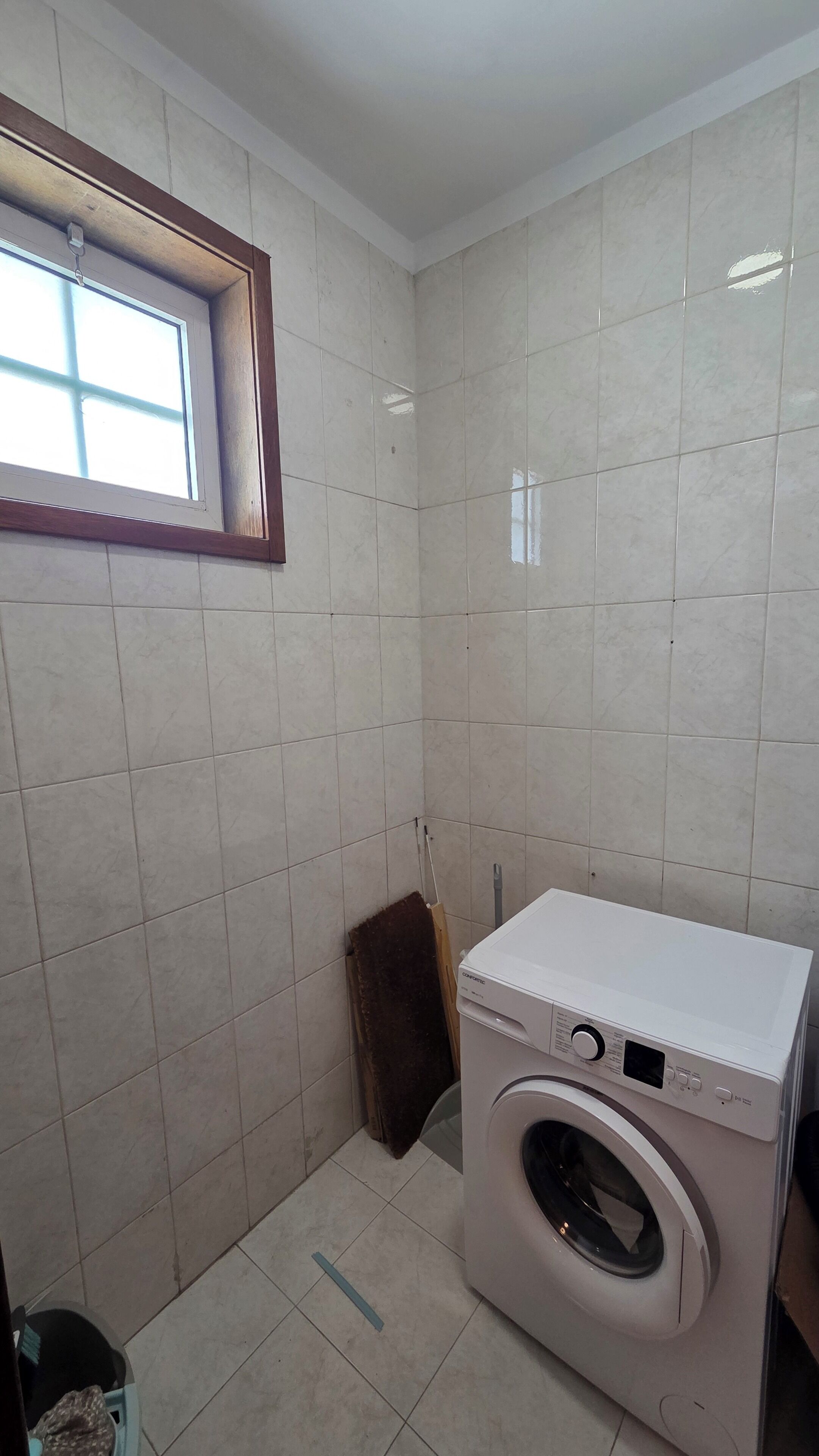 A laundry room with a washing machine, a window, and tiled walls.