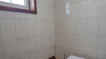 A laundry room with a washing machine, a window, and tiled walls.