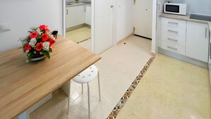 A modern kitchen with white cabinets, a microwave, and a wooden dining table with a vase of flowers. - Colina 10 Studio by Residea (Torremolinos)