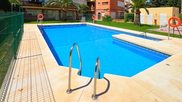 A swimming pool with two ladders, surrounded by a fenced area, and adjacent to a multi-story building with balconies. - Colina 10 Studio by Residea (Torremolinos)