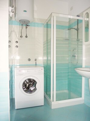 A compact bathroom with a washing machine, a glass shower enclosure, and a sink. - Relaxing Apartment Near the Beach (San Michele al Tagliamento)