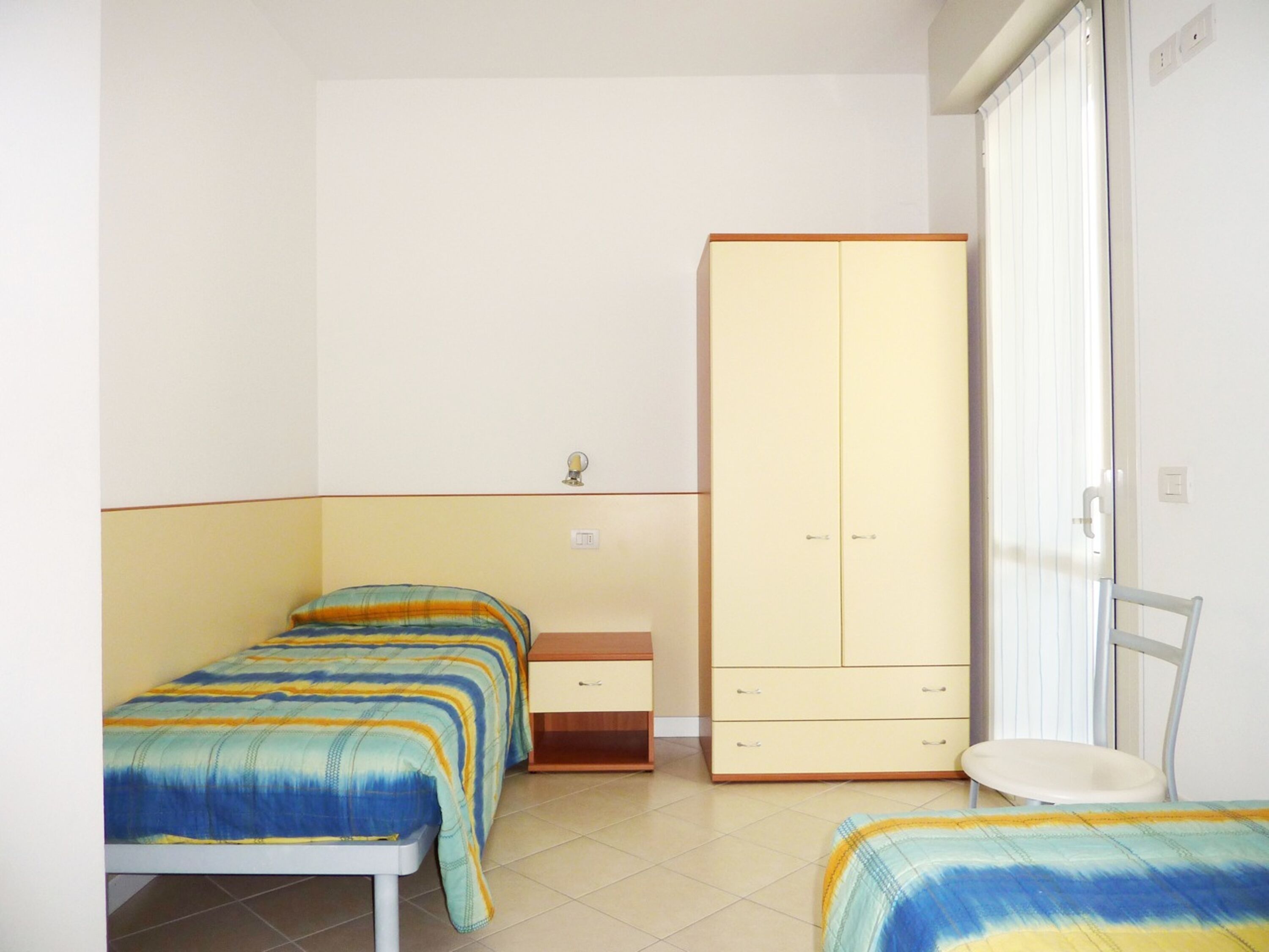 Un dormitorio con dos camas individuales, un armario, una mesita de noche y una silla.