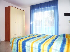 A bedroom with a bed, a wardrobe, and a window with blue curtains. - Relaxing Apartment Near the Beach (San Michele al Tagliamento)