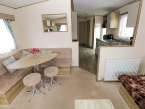 Un intérieur de camping-car compact comprenant un coin cuisine, un espace repas avec une table et deux chaises, un canapé et un banc recouvert de fourrure.