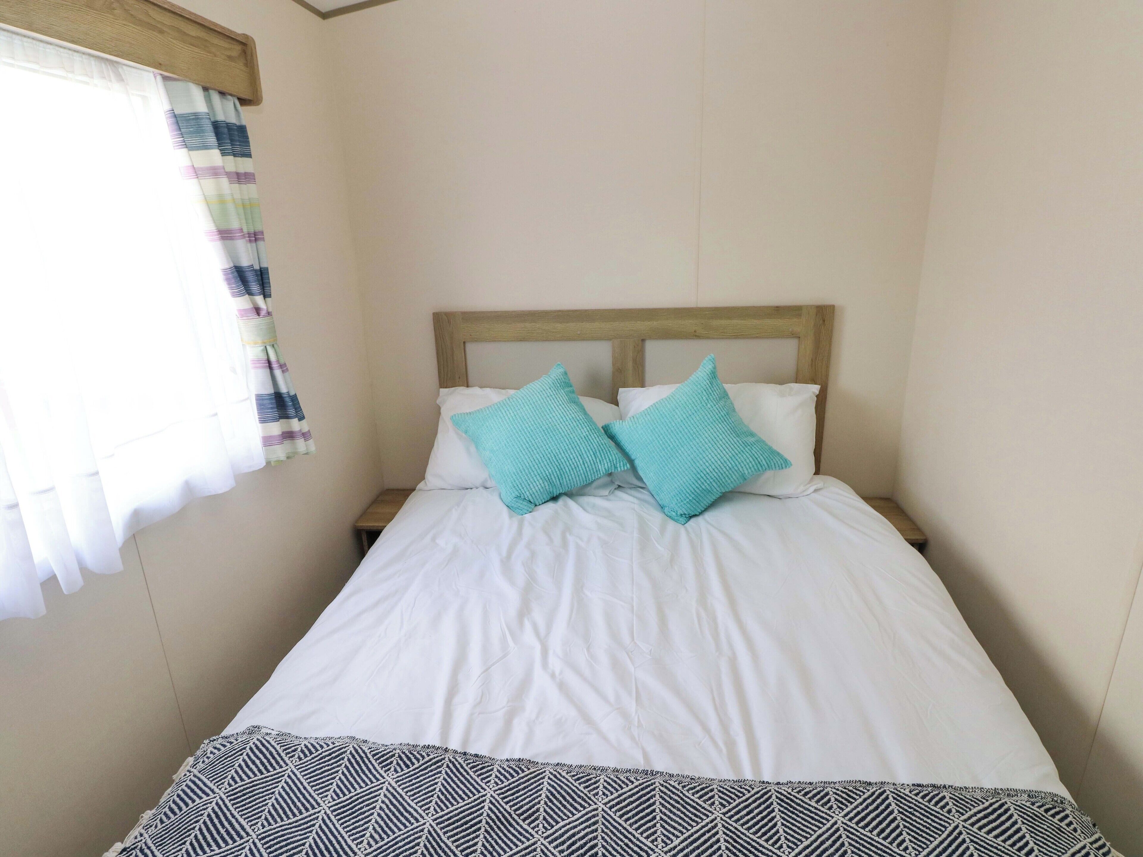 A bed with white bedding, two teal pillows, a wooden headboard, and a patterned throw at the foot of the bed.