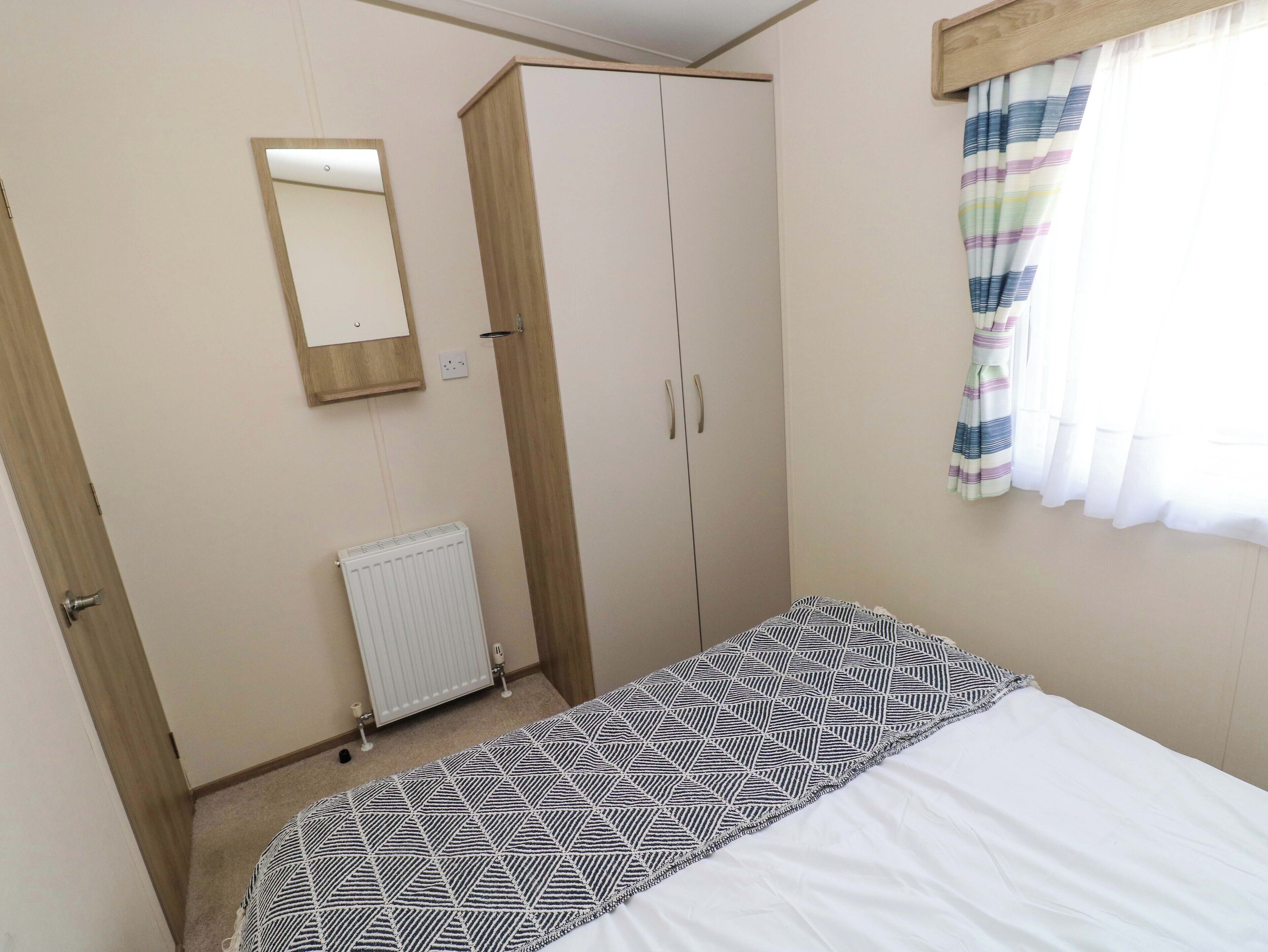 Une chambre à coucher avec un lit, une armoire, un radiateur et une fenêtre avec des rideaux.