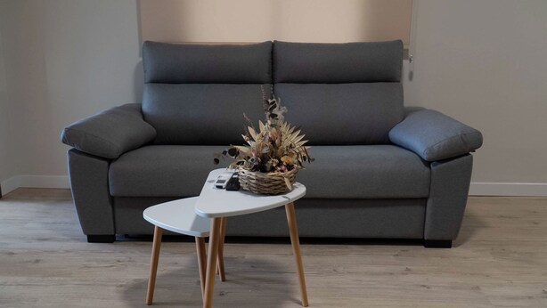 A grey sofa with a white side table in front, a wicker basket with dried flowers, and a remote control on the table. - Apartment in the center of Padrón 2 (Padrón)