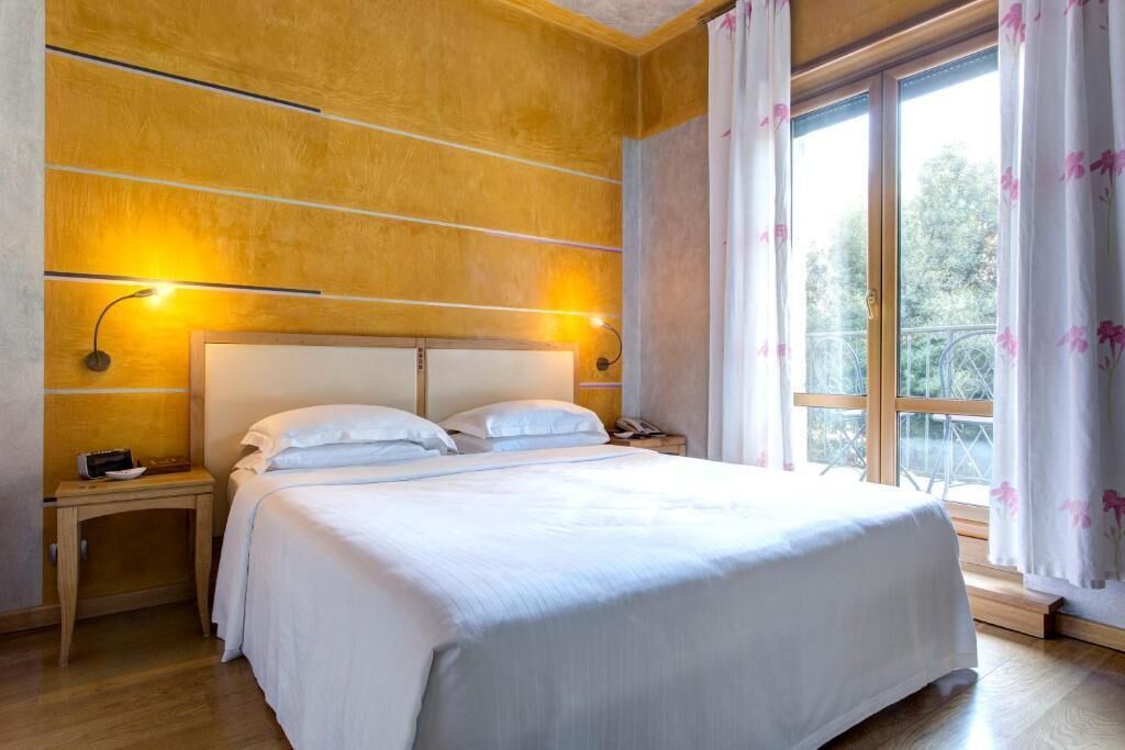 A bedroom with a large bed, wooden walls, a nightstand with a lamp, and a window with curtains.