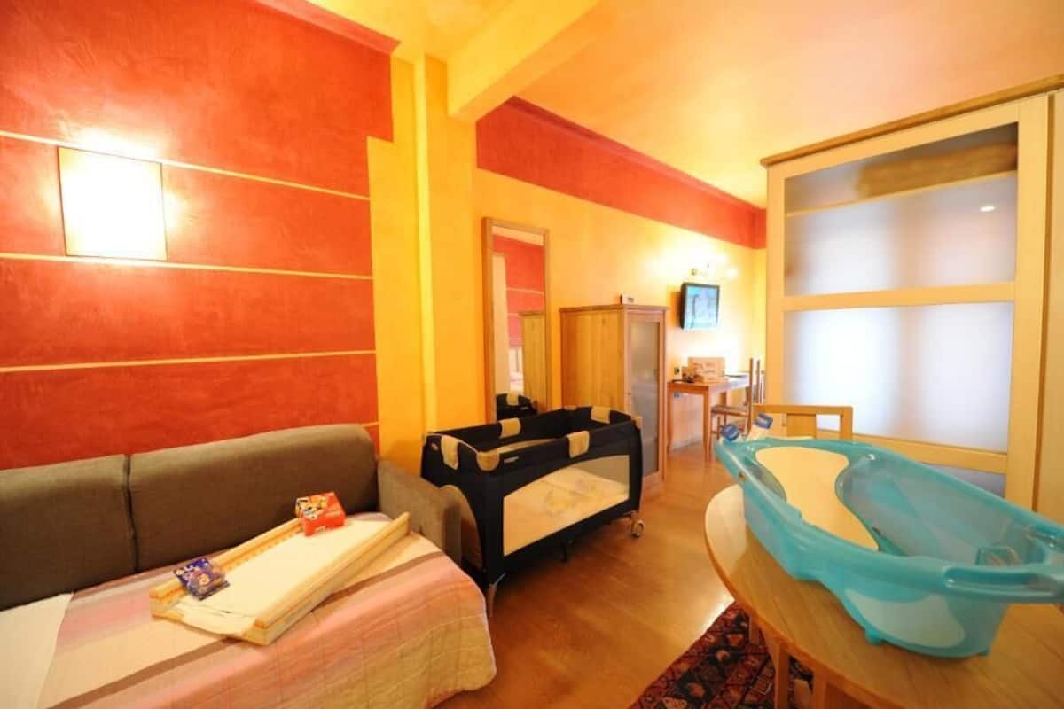 Habitación de hotel con sofá, cuna, bañera y una mesita con bandeja.