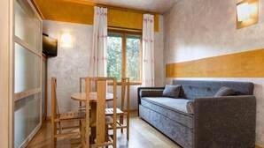 Una habitación con una mesa y sillas de madera, un sofá gris, una ventana con cortinas y una lámpara fijada a la pared.