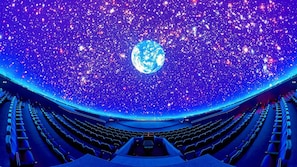 An indoor cinema with rows of seats and a large screen displaying a planet. - Socrates Path (Athens)