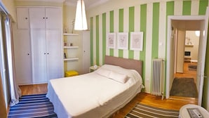 Un dormitorio con cama, armario, mesita de noche, lámpara y radiador.