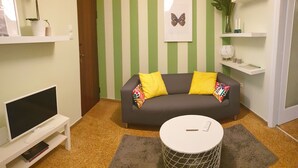 Una sala de estar con un sofá gris, cojines amarillos, un mueble blanco para televisión y una mesita redonda blanca.