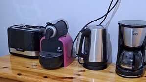 A wooden chest of drawers with a toaster, a coffee maker, and a kettle on top.