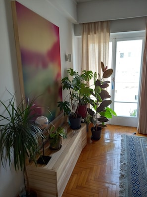 A room with a wooden bench, potted plants, a large abstract painting, and a patterned rug. - Acropolitana Grand View Veranda (Athens)