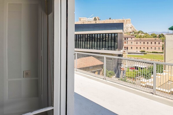 A balcony with a view of a building with solar panels, a courtyard, and a distant hill. - Acropolitana Grand View Veranda (Athens)