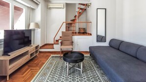 Una sala de estar moderna con un mueble de televisión de madera, un sofá gris, un tapete estampado, una silla negra y una escalera con barandilla de madera.