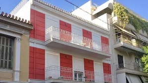 Un edificio de varios pisos con balcones, un coche estacionado al frente y un pequeño árbol en el jardín delantero.