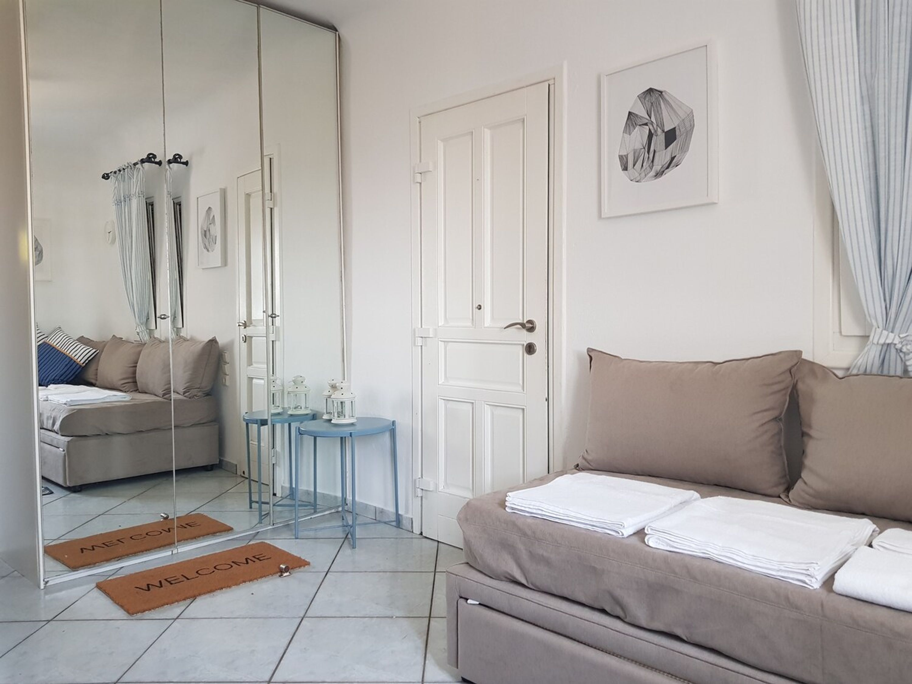 Een moderne slaapkamer met een grote spiegel, een bank, een klein tafeltje met lantaarns, en een deur met een afbeelding op de muur.